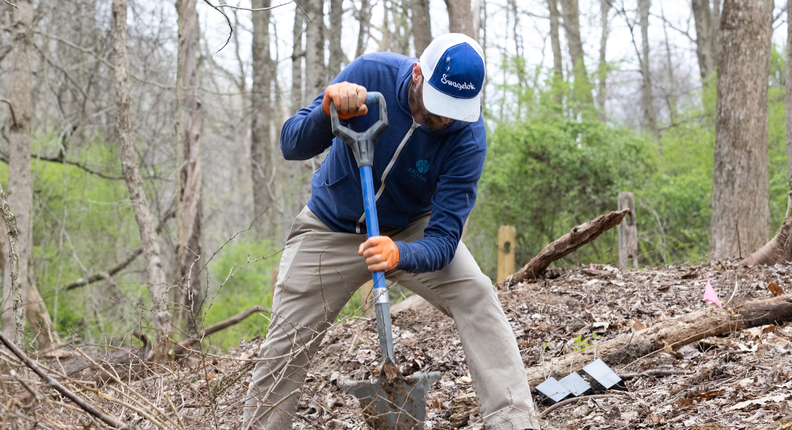 Man digging a hole for a tree during a volunteer planting in a wooded park area